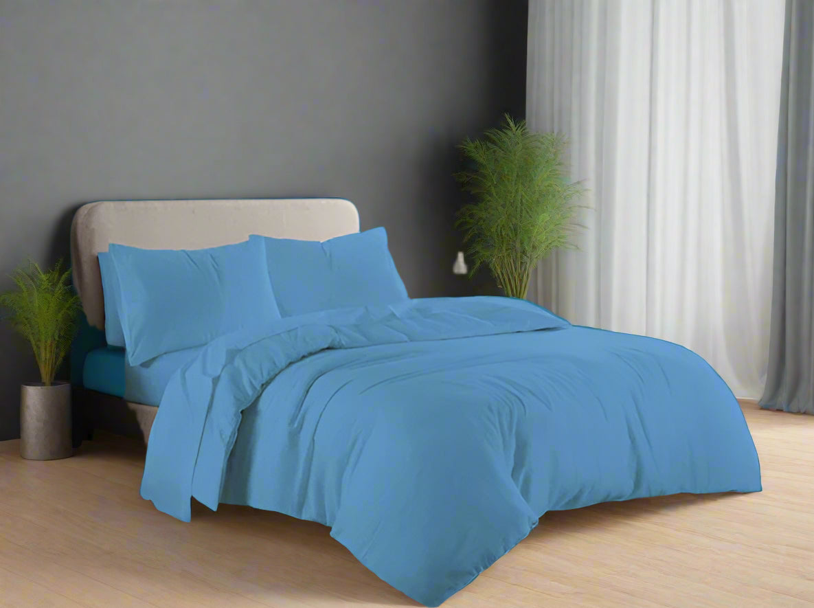 Blue bedding set on a bed in a well-lit room with a window in the background.