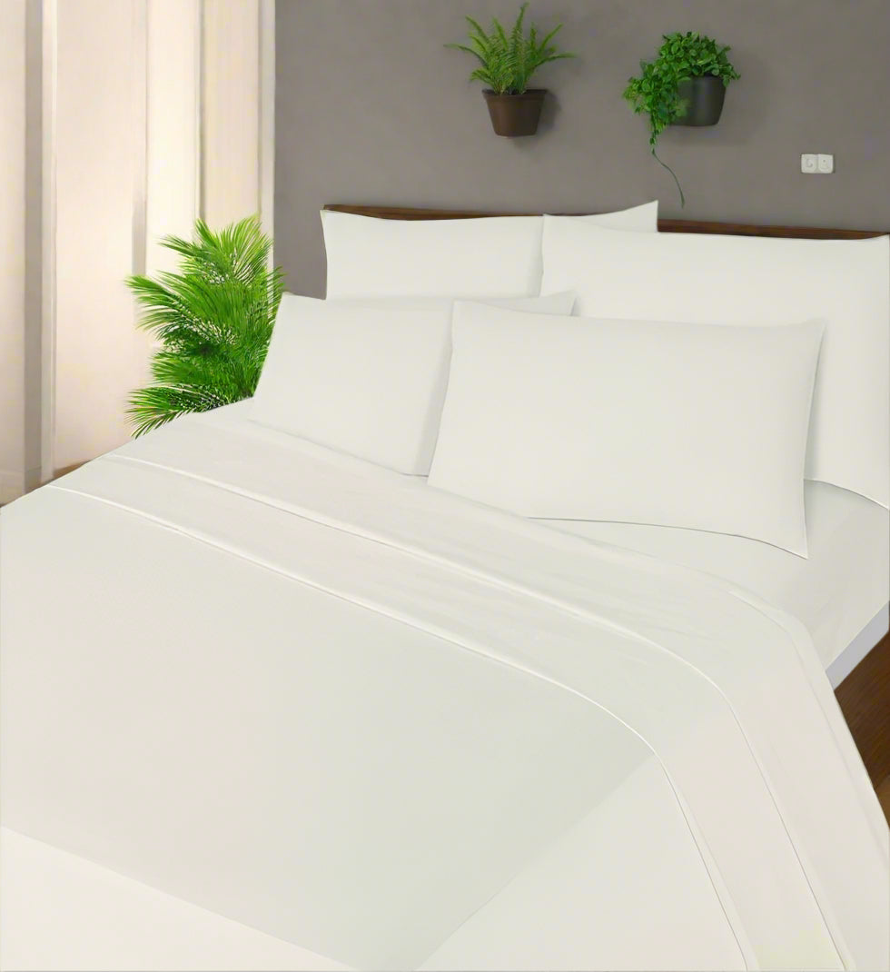 White bedding set on a bed with a nightstand and lamp in a bedroom.