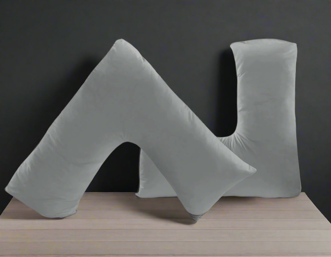 Gray U-shaped pillows on a white bed with a light gray wall and small plant in the background.