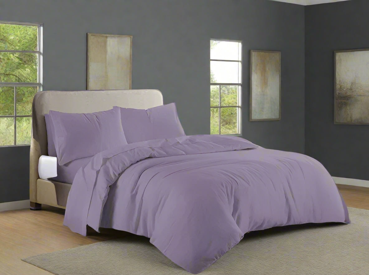 Purple bedding set on a bed in a bedroom with a dresser and window.