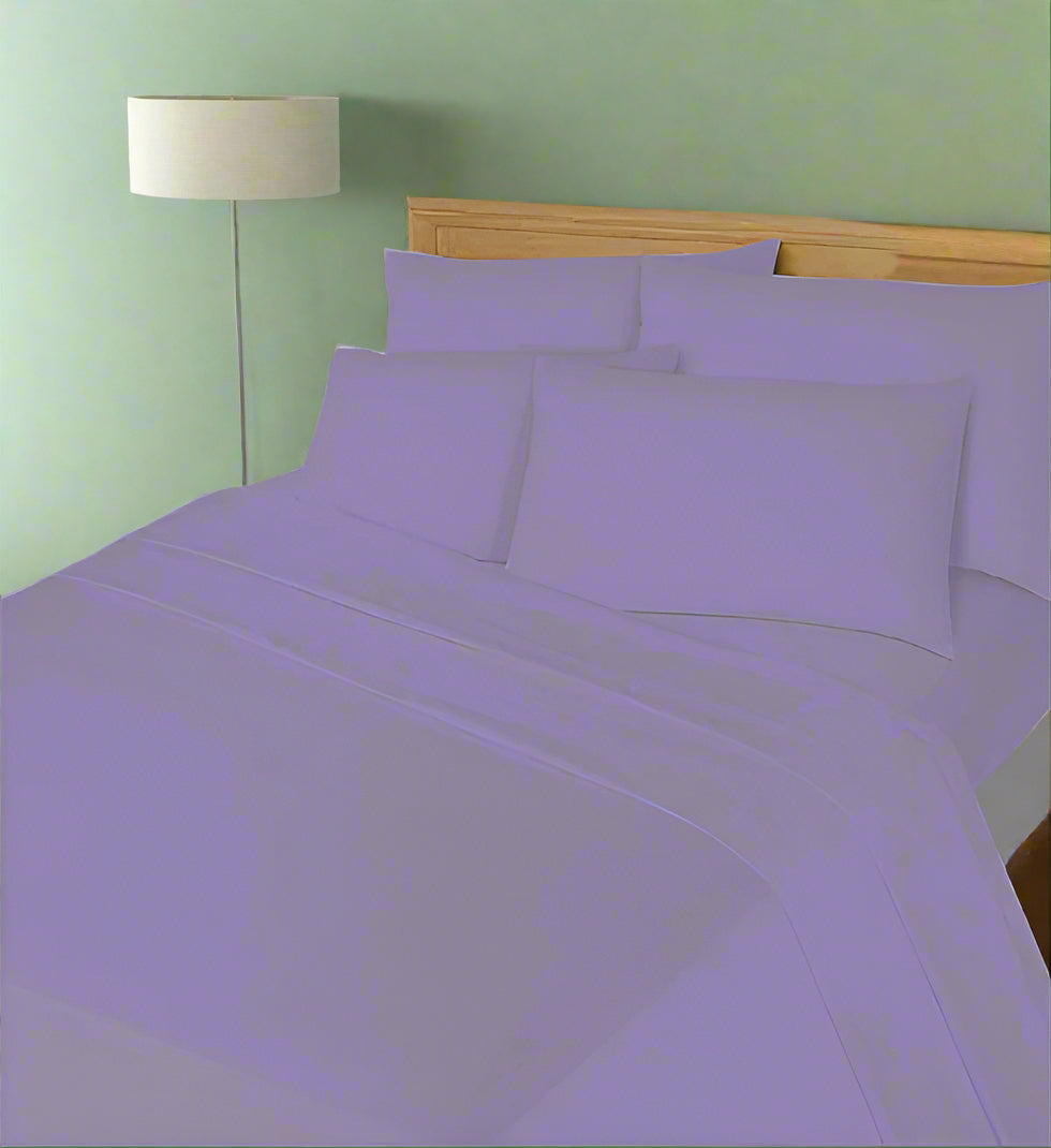 Purple bedding set on a bed with a wooden headboard and lamp in the background.