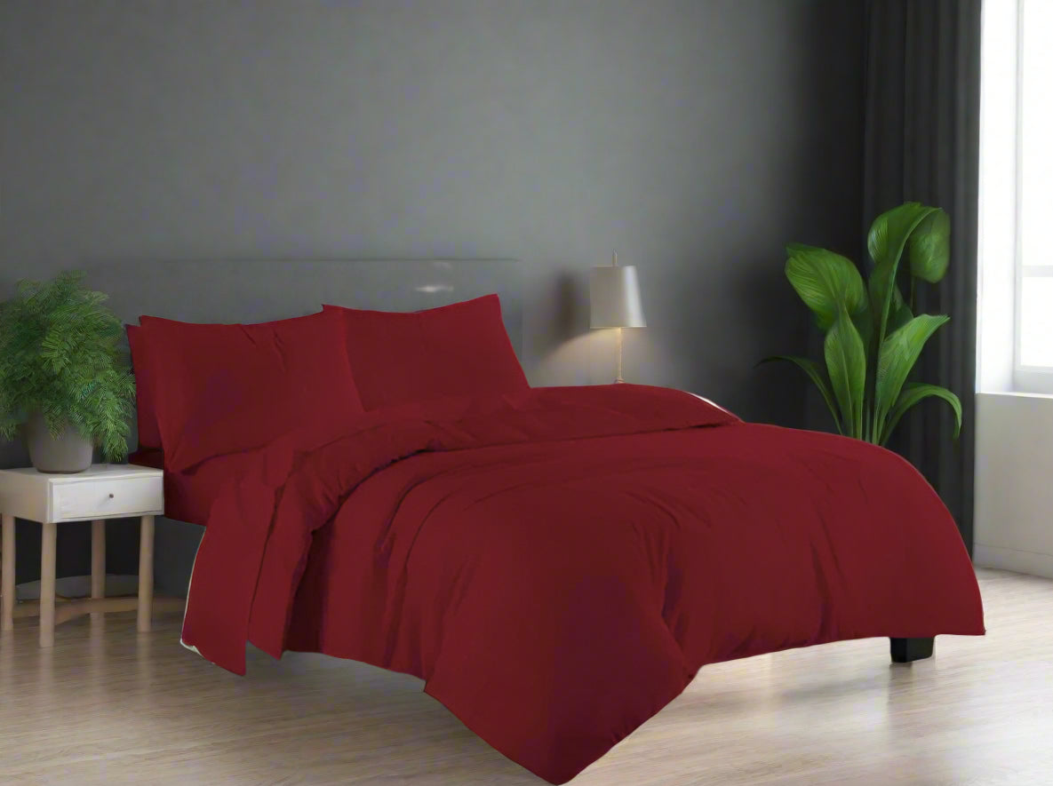 Red bedding set on a bed in a well-lit bedroom with white furniture and decor.