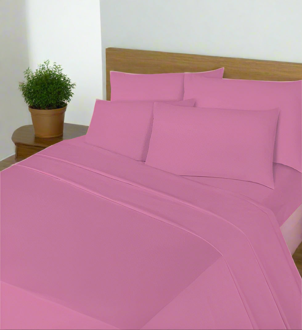 Pink bed sheets and pillowcases on a bed with a white nightstand and lamp in the background.