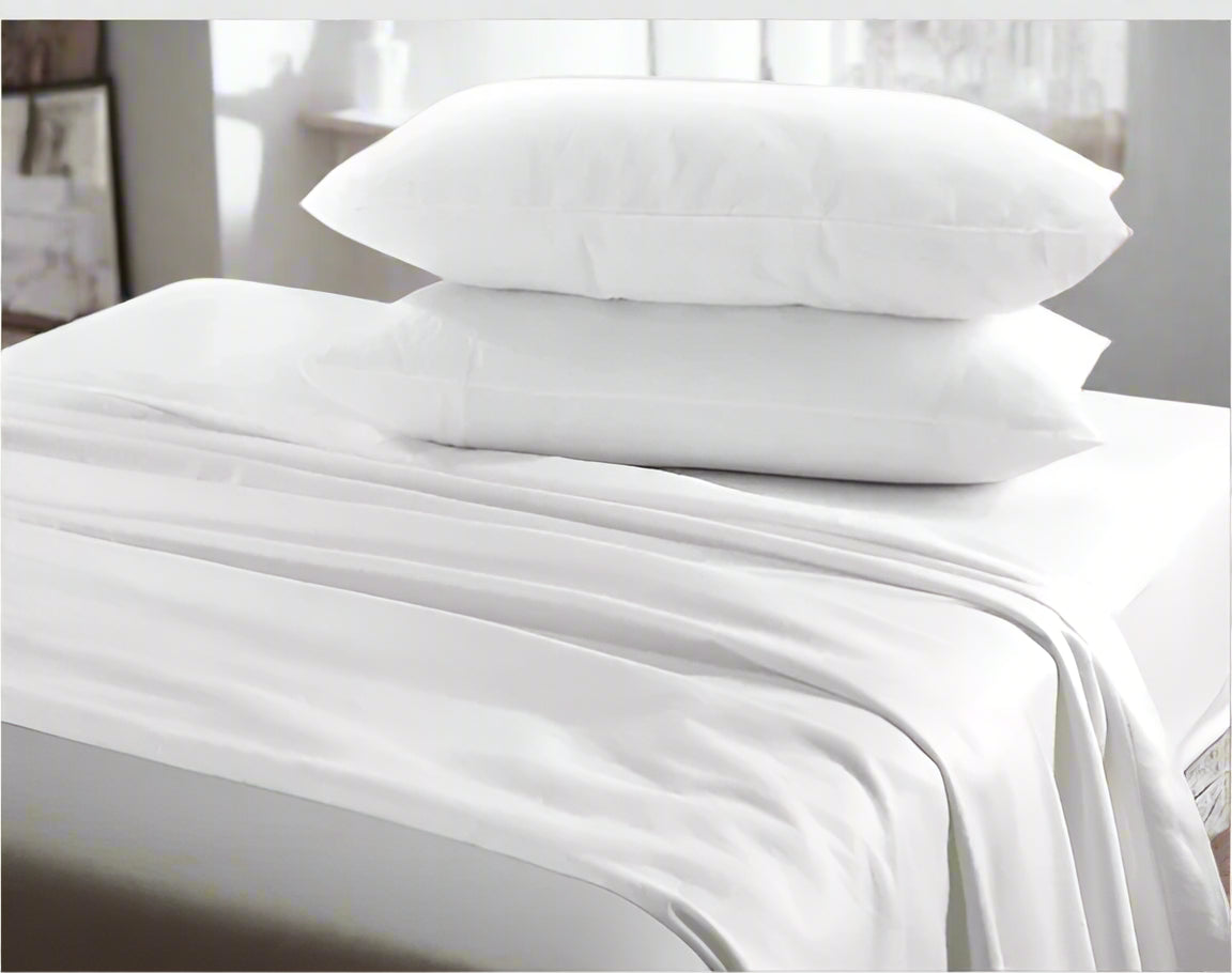 White bed sheets and pillows on a bed with a neutral headboard.
