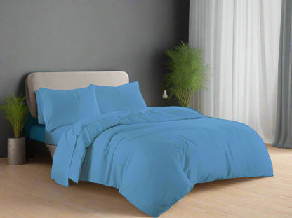 Blue bedding set on a bed in a well-lit room with a window in the background.