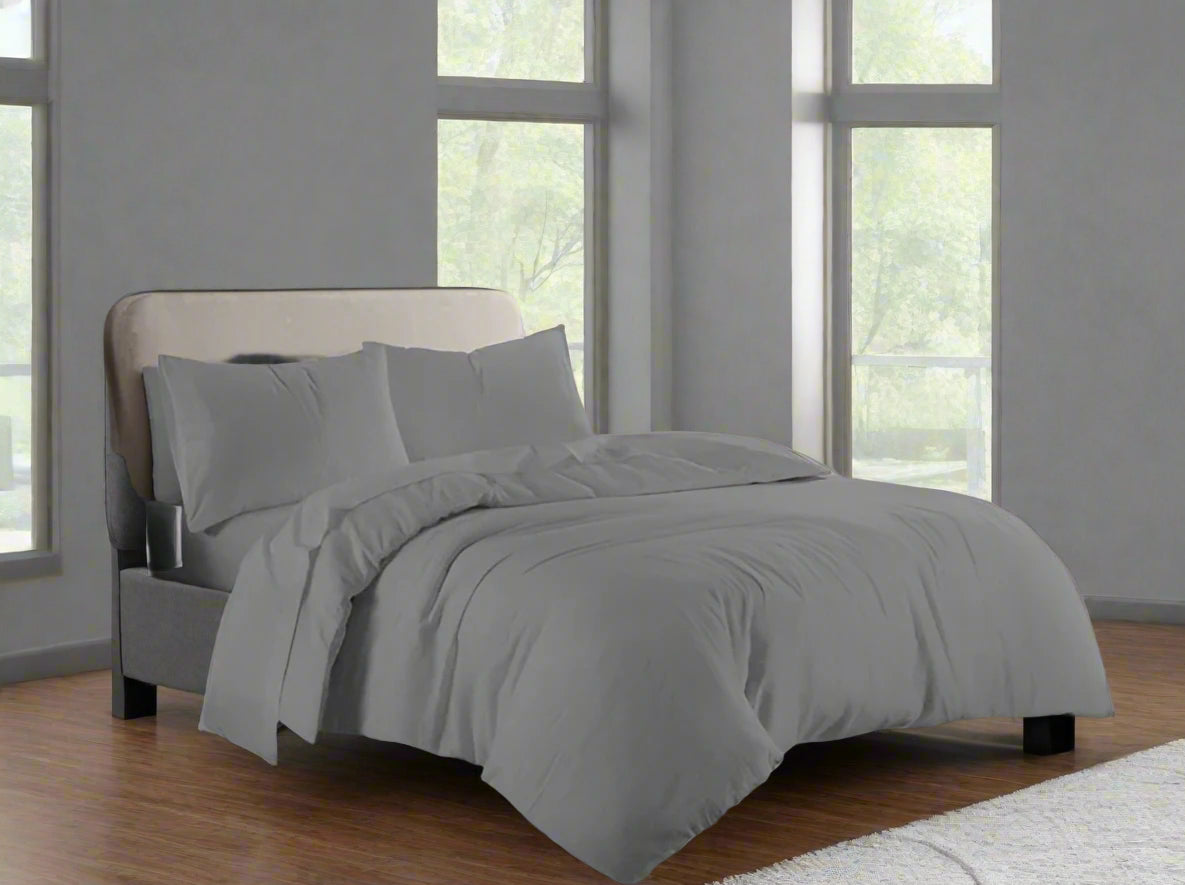 Gray bedding set on a bed in a room with large windows.