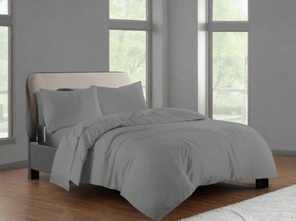 Gray bedding set on a bed in a room with large windows.