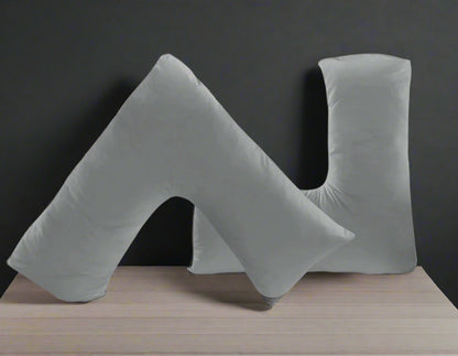 Gray U-shaped pillows on a white bed with a light gray wall and small plant in the background.