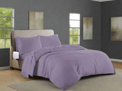 Purple bedding set on a bed in a bedroom with a dresser and window.