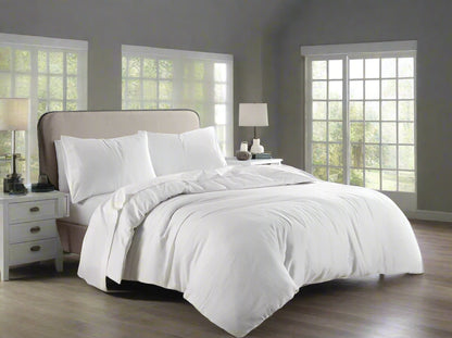 White bedding set on a bed in a bright bedroom with large windows.