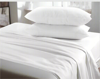 White bed sheets and pillows on a bed with a neutral headboard.